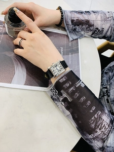 Elegant rectangular silver watch with black leather strap and Roman numerals on a magazine