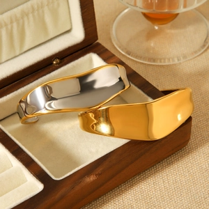 Polished 18K gold and silver wide stainless steel open bracelets on a wooden jewelry box