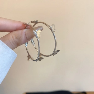 Detail of silver hoop earrings featuring frosted butterfly charms held by fingers