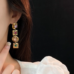 Detail of vintage baroque gold drop earrings with colorful gemstones and hammered metal texture