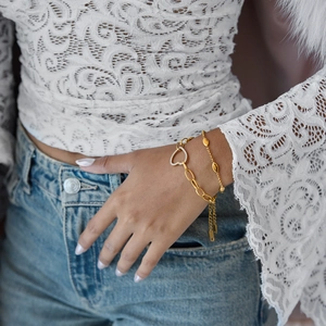Gros plan d'un mannequin portant des bracelets superposés en or 18K avec cœur et perles