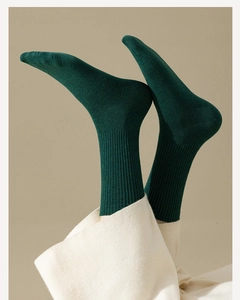 Close-up of dark green ribbed cotton socks worn by a model against a beige background