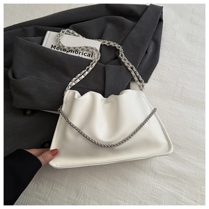 Close-up of a white pleated PU leather handbag with a silver metal chain on a grey blazer