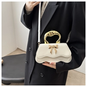 Close-up of white handbag with gold metallic handle and bow detail on model
