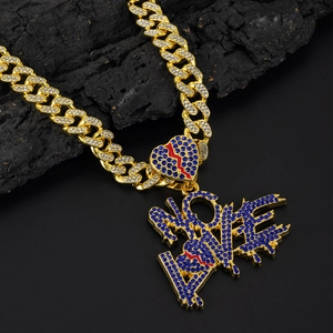 Detail of gold Cuban chain with blue rhinestone LOVE pendant and red broken heart on charcoal