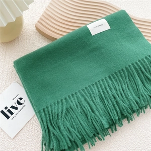Detail of grass green scarf with soft fringe edges and minimalist label on wooden tray