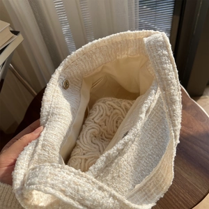 Détail de la texture tissée et du fermoir magnétique sur le sac en tweed crème
