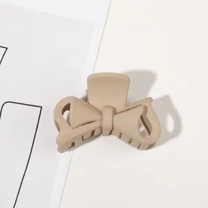Detail of a matte beige bow-shaped hair claw clip with minimalist hollow line design