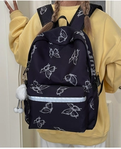 Close-up of black butterfly backpack with white plush ball charm on a yellow hoodie