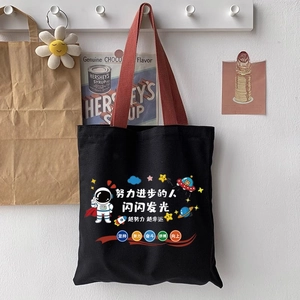 Detail of black canvas tote with red handles featuring a cartoon astronaut and ship