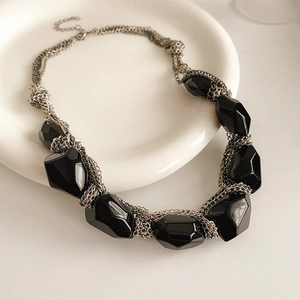 Close-up of irregular oval black geometric stones on silver chain necklace on ceramic plate