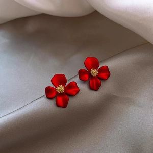 Macro detail of red matte flower earrings with golden core on silver silk fabric