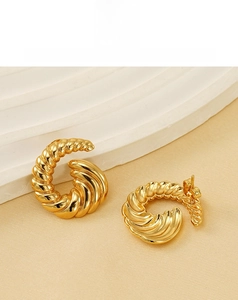 Macro shot of gold-plated spiral hoop earrings on a minimalist textured background
