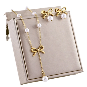 Elegant gold bow necklace and pearl stud earrings jewelry set displayed on a grey box