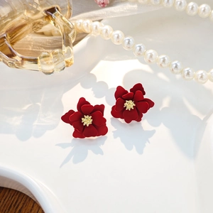 Detail of red matte flower earrings with golden stamen on a white decorative plate