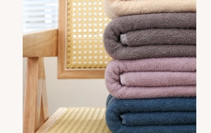 Close-up of stacked thick cotton towels in beige, grey, purple and navy on a rattan chair