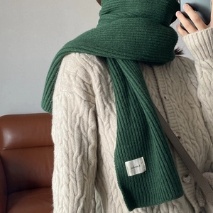 Thick dark green knit scarf with small white label shown in a cozy autumn winter style