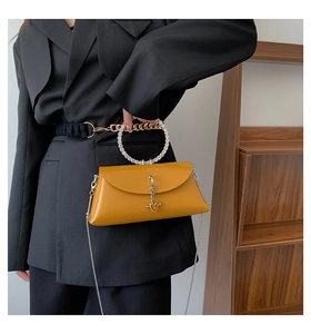 Close-up of mustard yellow handbag featuring a crystal-encrusted round handle and metal chain