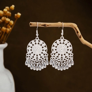 Silver bohemian leaf tassel earrings with mandala engraving on textured wood background