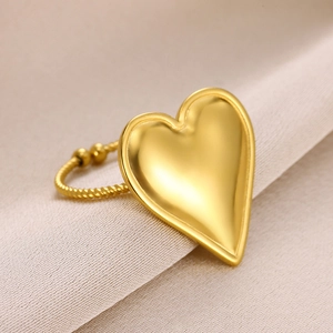 Macro detail of 18k gold heart ring with braided band on beige fabric background