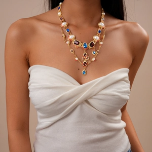 Detail view of a multi-layer vintage necklace with red gems and pearls on a female model