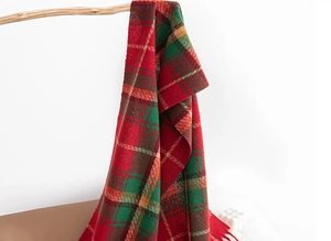 Detail of red and green plaid scarf with soft fringe hanging on a wooden branch
