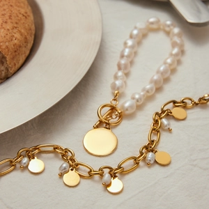 Elegant 18K gold coin and white freshwater pearl bracelet set on a brunch table scene