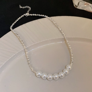 Detail of silver square chain necklace with white pearls on a ceramic plate