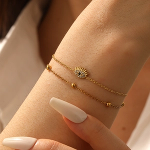 Detail of double-layer gold chain bracelet with crystal evil eye charm on wrist