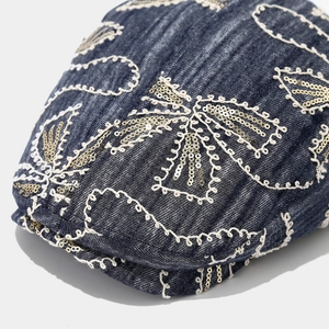 Detail of dark blue denim flat cap with white wavy embroidery and golden sequins