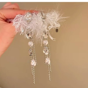 Détail de boucles d'oreilles avec plumes blanches, dentelle, cristaux et pompons perles