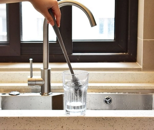 Primo piano di uno scopino in silicone grigio a manico lungo che pulisce un bicchiere