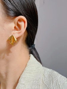 Detailed view of irregular geometric gold stud earrings worn by a model in Roman art style