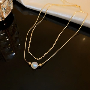 Close-up of double-layered gold necklace with square link chain and a lustrous pearl pendant