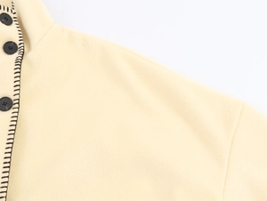 Detail of cream wool coat collar with black contrast stitching and round buttons
