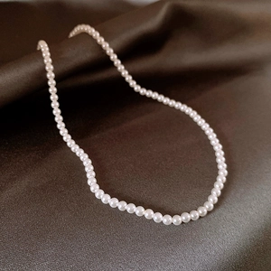 Classic round white pearl necklace with glossy finish on elegant brown silk fabric