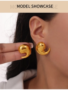 Close-up of a gold comma-shaped geometric stud earring worn by a model in soft studio lighting