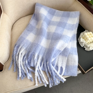 Detail of soft plaid scarf with tassels on beige sofa showing premium cashmere feel