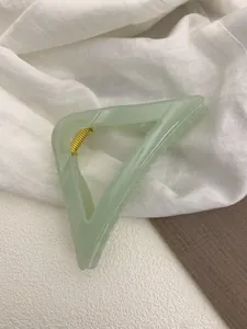Close-up of translucent mint green triangular hair claw clip with golden metal spring
