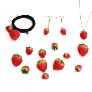 Flat lay of resin strawberry charms, handmade earrings, necklaces, and hair accessories
