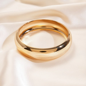 Detailed view of wide gold mirror-polished bangle on draped off-white silk background
