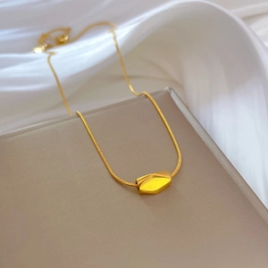 Macro shot of gold geometric pendant on a thin chain over soft silk background