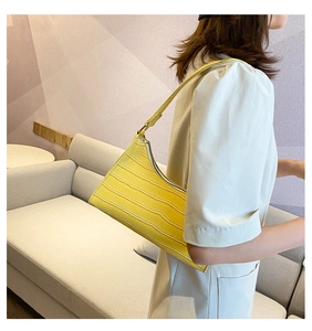 Detail of yellow crocodile pattern leather underarm bag worn by model in a home setting