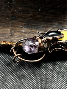Macro shot of beetle pendant featuring purple raw crystal and wire wrapped bronze detail