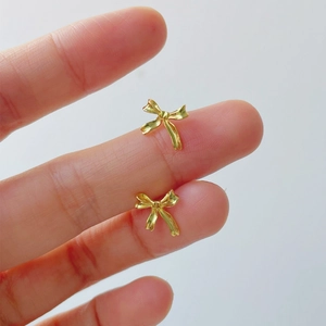 Elegant gold bow stud earrings shown on fingertips for size comparison and minimalist style
