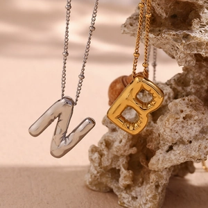 Macro shot of 18K gold and silver balloon letter pendants on smooth natural rock background