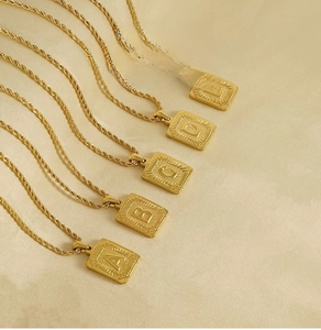 Détail de pendentifs carrés à lettres en acier doré sur des chaînes torsadées
