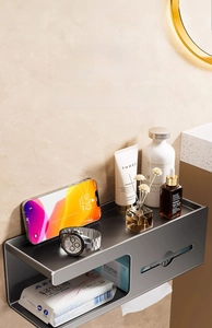 Close-up of wall-mounted tissue box with storage shelf holding phone and accessories