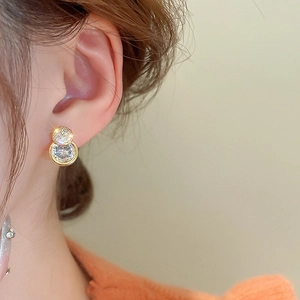 Detailed close-up of a zircon round earring in gold plating on a female model