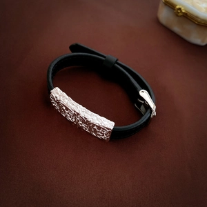 Detailed view of black leather bracelet with engraved silver buckle on dark fabric